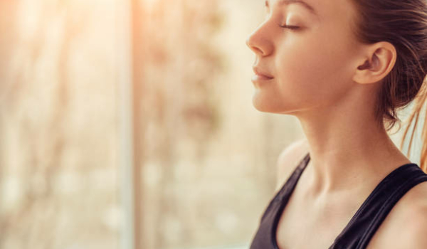 Side view of young female with closed eyes breathing deeply while doing respiration exercise during yoga session in gym