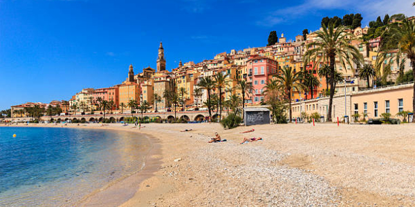 Menton, France - May 26, 2014: People sunbathing on the large beach of Menton, a beautiful town facing the Mediterranean Sea in southeastern France. Its warm microclimate allows people to sunbathe even in spring.